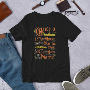 A black short sleeved T-shirt laying flat with objects around it. The T-Shirt features hand lettering with the CS Lewis quote "Once a king or queen of Narnia, always a king or queen of Narnia."