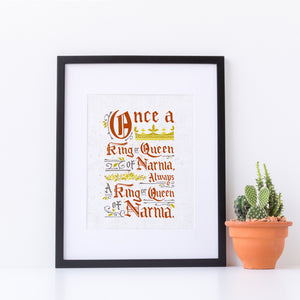 Artwork in a black frame with the with a white matte. The frame is leaning on a white counter. The artwork features hand drawn lettering of the Narnia quote "Once a king or queen of Narnia, always a king or queen of Narnia."