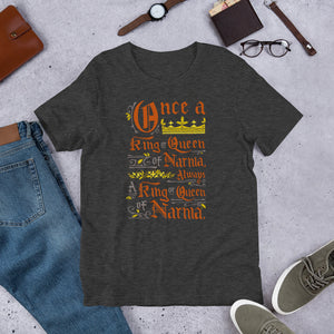A dark grey short sleeved T-shirt laying flat with objects around it. The T-Shirt features hand lettering with the CS Lewis quote "Once a king or queen of Narnia, always a king or queen of Narnia."