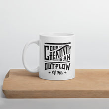 Load image into Gallery viewer, A white mug sitting on a piece of wood. The white mug features hand drawn lettering with the words &quot;Our creativity is an outflow of His.&quot; The words are in black.