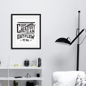 Artwork featured on a wall in a black frame by a shelving unit. The artwork is on white paper and features hand drawn lettering with the words "Our creativity is an outflow of His." The words are in black. 