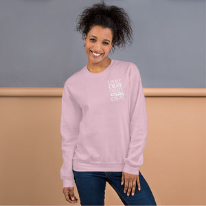 A woman wearing a light pink sweatshirt with the word "create, create, create, create, create" in white in a small rectangle on the upper left side.
