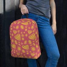 Load image into Gallery viewer, A woman leaning on a black fence with just her hands, waist and jeans showing. She is holding a backpack by its top loop strap. The backpack features illustrated gems and diamonds in gold on top off a muted hot pink colored backpack. 