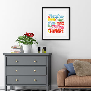 Artwork in a black frame featured in a room with the words “A teacher takes a hand, opens a mind, and touches a heart.” The “a” in the word “heart” is a heart shape and the words are blue, red, yellow and green. 