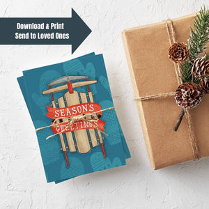 A stack of Christmas cards with brown string wrapped around them. A brown craft paper gift is off to the side. The card has a blue background with lighter blue winter mittens in a pattern. On top of the mittens is an illustrated vintage sled with red ribbon and the words "season's greetings" in white. The words "download & print, send to loved ones" is in the upper lefthand corner of the image.