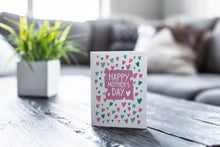 Load image into Gallery viewer, A greeting card is on a table top with a yellow plant pot and a green plant inside. The card features the words  “Happy Mother’s Day” with illustrated hearts around the words. 