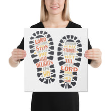 Load image into Gallery viewer, A woman holding a canvas in her hands. The artwork features illustrated footprints in black with the words in grey, yellow and orange. The words read &quot;The Lord makes firm the steps of the one who delights in him. Though he may stumble, he will not fall, for the Lord upholds him with his hand.&quot;