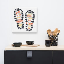 Load image into Gallery viewer, A canvas shown on a wall of a kitchen. The artwork features illustrated footprints in black with the words in grey, yellow and orange. The words read &quot;The Lord makes firm the steps of the one who delights in him. Though he may stumble, he will not fall, for the Lord upholds him with his hand.&quot;