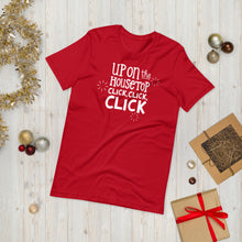 Load image into Gallery viewer, A red T-shirt laying on the ground with Christmas items surrounding it. The T-shirt features the words  &quot;Up on the housetop, click, click, click&quot; in white. There are three stars around the words in white. 