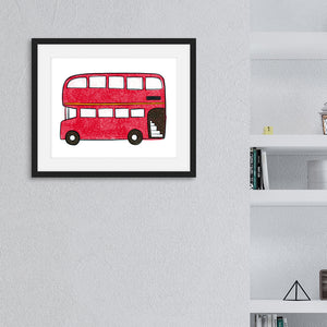 An illustration of a red, double decker bus in a black frame. The frame is hanging on the wall next to a bookshelf.