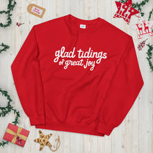 Load image into Gallery viewer, A red sweatshirt laying on a table with Christmas objects around it. The sweatshirt has the words &quot;glad tidings of great joy&quot; in white. 