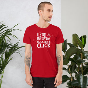 A man wearing a red short sleeved t-shirt. The tee features lettering of the words "Up on the housetop, click, click, click." The words are in white with three stars in white surrounding the words. 