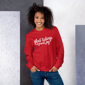 A woman wearing a red sweatshirt featuring hand drawn lettering with the words "glad tidings of great joy" in white. 