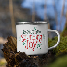 Load image into Gallery viewer, White enamel mug sitting on top of a tree branch with moss in the background. The design on the mug is featured in red and green reading &quot;Repeat the Sounding Joy&quot; with musical notes around the words. 