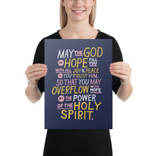Load image into Gallery viewer, A woman holding a canvas in her hands. The canvas is purple and features hand drawn text in white, pink and yellow reading &quot;May the God of hope fill you with all joy and peace as you trust him, so that you may overflow with hope by the power of the holy spirit.&quot; 