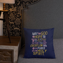 Load image into Gallery viewer, A pillow leaning on a grey headboard with a plant in the background. The purple pillow features hand drawn lettering of the Bible verse &quot;May the God of hope fill you with all joy and peace as you trust him, so that you may overflow with hope by the power of the holy spirit.&quot; The lettering in white, pink and yellow. 