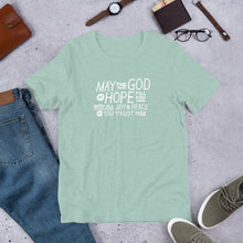 Load image into Gallery viewer, A short sleeved T-shirt laying flat with objects around it. The tee is heather prism dusty blue and features hand drawn lettering in white with the words &quot;May the God of hope fill you with all joy and peace as you trust him.&quot;