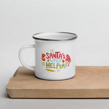 Load image into Gallery viewer, A white enamel mug sitting on top of a wood cutting board on a white background. The mug is white with the very top silver enamel. The design features hand illustrated words reading &quot;Santa&#39;s Little Helper&quot; with cute baking illustrations around the words. The design on the mug is in red, light blue and green. 