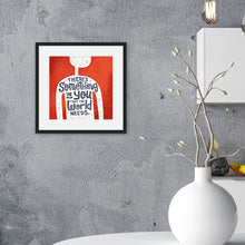 Load image into Gallery viewer, A red print in a black frame hangs on a textured grey kitchen wall. The print features the outline of a person in white, filled with light grey doodles. The words ‘There’s something in you the world needs&#39; are lettered in black across the person’s chest. In the background there are white kitchen cabinets and a large white vase.
