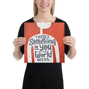 A smiling woman holds a small red art canvas. The canvas design features the outline of a person in white, filled with light grey doodles. The words ‘There’s something in you the world needs' are lettered in black across the person’s chest.