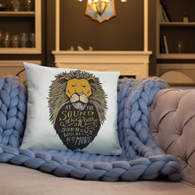 Load image into Gallery viewer, A white square pillow shown on a blue crochet blanket sitting on a sofa in a living room. The pillow artwork features hand drawn illustration of the Chronicles of Narnia lion character Aslan. Inside the illustration there is the quote “At The Sound of Your Roar, Sorrows Will Be No More.”