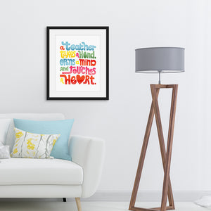 Lettering artwork is featured in a black from above a sofa. The artwork has the phrase  “A teacher takes a hand, opens a mind, and touches a heart.” The “a” in the word “heart” is a heart shape and the words are blue, red, yellow and green. 