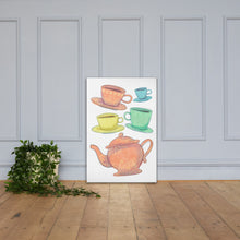 Load image into Gallery viewer, A canvas is leaning against a light grey wall with a plant next to it on the floor. The artwork is on a white background with four teacups on saucers and one large teapot. The teacups are in muted colors of orange, blue, yellow and green and the teapot is a muted orange. On the teacups, saucers and teapot there is a light flower detail pattern.