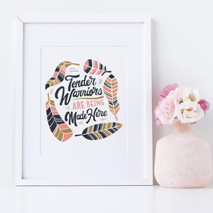 Artwork in a white frame with the with a white matte. The artwork is on a white background with lettering reading "Tender Warriors Are Being Made Here" The words are in pink, navy and dark mustard yellow. 