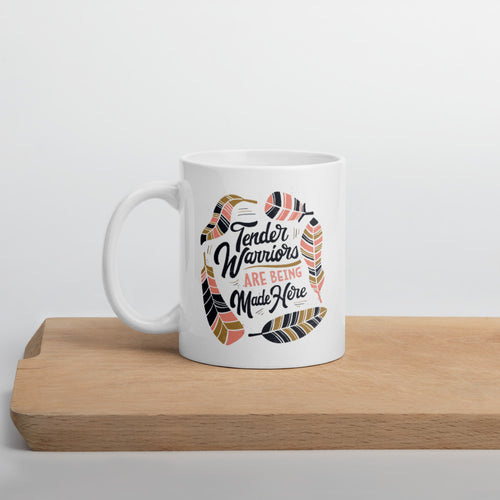 A white mug sitting on a piece of wood. The white mug features hand drawn lettering with the words 