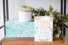 Load image into Gallery viewer, A greeting card is on a table top with a present in blue wrapping paper in the background. On top of the present is a candle and some greenery from a plant too. The card features illustrated plant leaves around the words “Thank you Mum.”