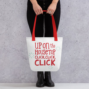 Someone holding a tote bag with red handles and a white fabric bag. The artwork is in red saying "Up on the housetop, click, click, click" with blue stars around the words. 