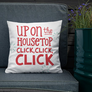 The white pillow is leaning on a sofa with a plant off to the side. The pillow is white and has the words in red saying "Up on the housetop, click, click, click." There are three blue stars around the words. 
