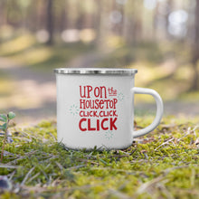 Load image into Gallery viewer, A white enamel mug with a silver enamel rim sitting in the grass. The illustrated design says &quot;Up on the housetop, click, click, click&quot; in red with small blue stars around it. 