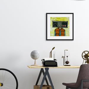 A black frame hanging above a desk featuring artwork with the original Nintendo controller as a "head" on a person wearing an orange puffer vest. 