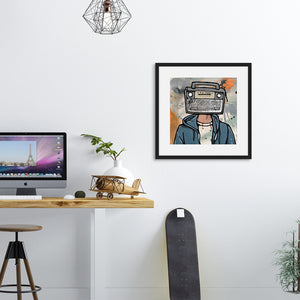 A black frame on a wall next to a desk with a computer. The artwork in the frame features a vintage boombox as the head of a person. 