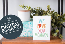Load image into Gallery viewer, A greeting card is on a table top with a present in blue wrapping paper in the background. On top of the present is a candle and some greenery from a plant too. The card features the words “We Love You Mommy!” The words &quot;digital download&quot; are featured in a circle on top of the image. 