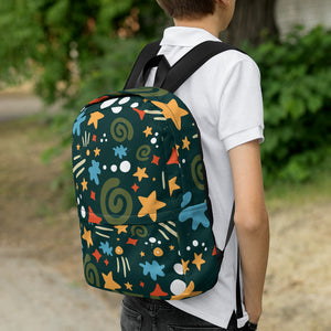 A boy faced with back to camera and a backpack on his shoulders. The backpack is a hunter green with a fun pattern of yellow stars, greens swirls, blue "splats" and other fun whimsical shapes. 