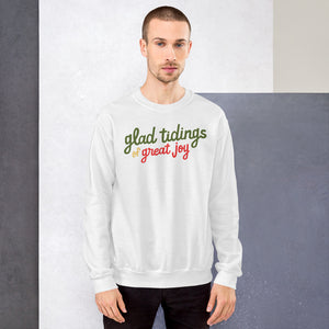 A man wearing a white sweatshirt featuring hand drawn lettering with the words "glad tidings of great joy" in red, green and yellow. 