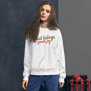 A woman wearing a white sweatshirt featuring hand drawn lettering with the words "glad tidings of great joy" in red, green and yellow. 
