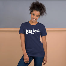 Load image into Gallery viewer, A woman wearing an navy short sleeved t-shirt. The tee features lettering of the word &quot;Believe&quot; in white with the &quot;I&quot; of the word featured as an illustrated Christmas tree. 