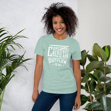 Load image into Gallery viewer, A woman wearing a Heather Prism Dusty Blue short sleeved t-shirt. The tee features hand drawn lettering featuring the words &quot;Our creativity is an outflow of His&quot; in white letters.  