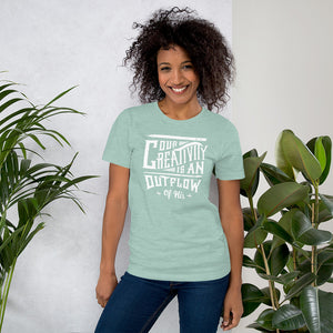 A woman wearing a Heather Prism Dusty Blue short sleeved t-shirt. The tee features hand drawn lettering featuring the words "Our creativity is an outflow of His" in white letters.  