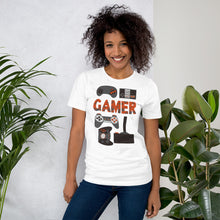 Load image into Gallery viewer, A woman wearing a white short sleeved t-shirt. The tee features hand drawn lettering and illustrations featuring different game controllers and the word &quot;gamer.&quot; The illustrations and gamer word are in red, grey and black. 