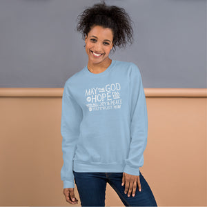 A woman wearing a light blue sweatshirt featuring hand drawn lettering in white with the words "May the God of hope fill you with all joy and peace as you trust him."