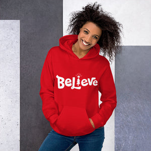 A woman wearing a red hoodie featuring hand drawn lettering in white with the word "Believe." The "I" of Believe is a Christmas tree illustration, also in white. 