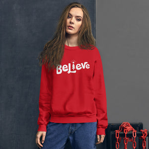 A woman wearing a red sweatshirt featuring hand drawn lettering with the word Believe. The "I" of the word Believe is an illustrated Christmas tree. 