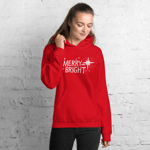 A woman wearing a red hoodie featuring hand drawn lettering in white with the words "Merry and Bright" with white illustrated stars around the words. 