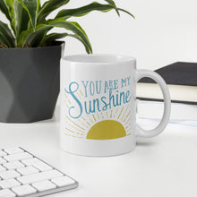 Load image into Gallery viewer, A white mug sits on a white desk beside a potted plant.  The mug reads &#39;You are my sunshine&#39; in blue over a yellow sun illustration