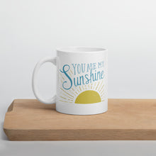Load image into Gallery viewer, A white mug sits on a wooden shelf.  The mug reads &#39;You are my sunshine&#39; in blue over a yellow sun illustration
