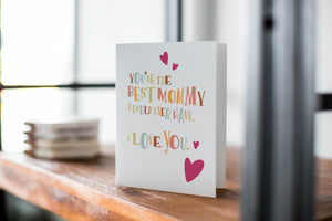 A card on a wood tabletop with an object in the background that is out of focus. The card features the words “You’re the best mommy I could ever have. I love you.”